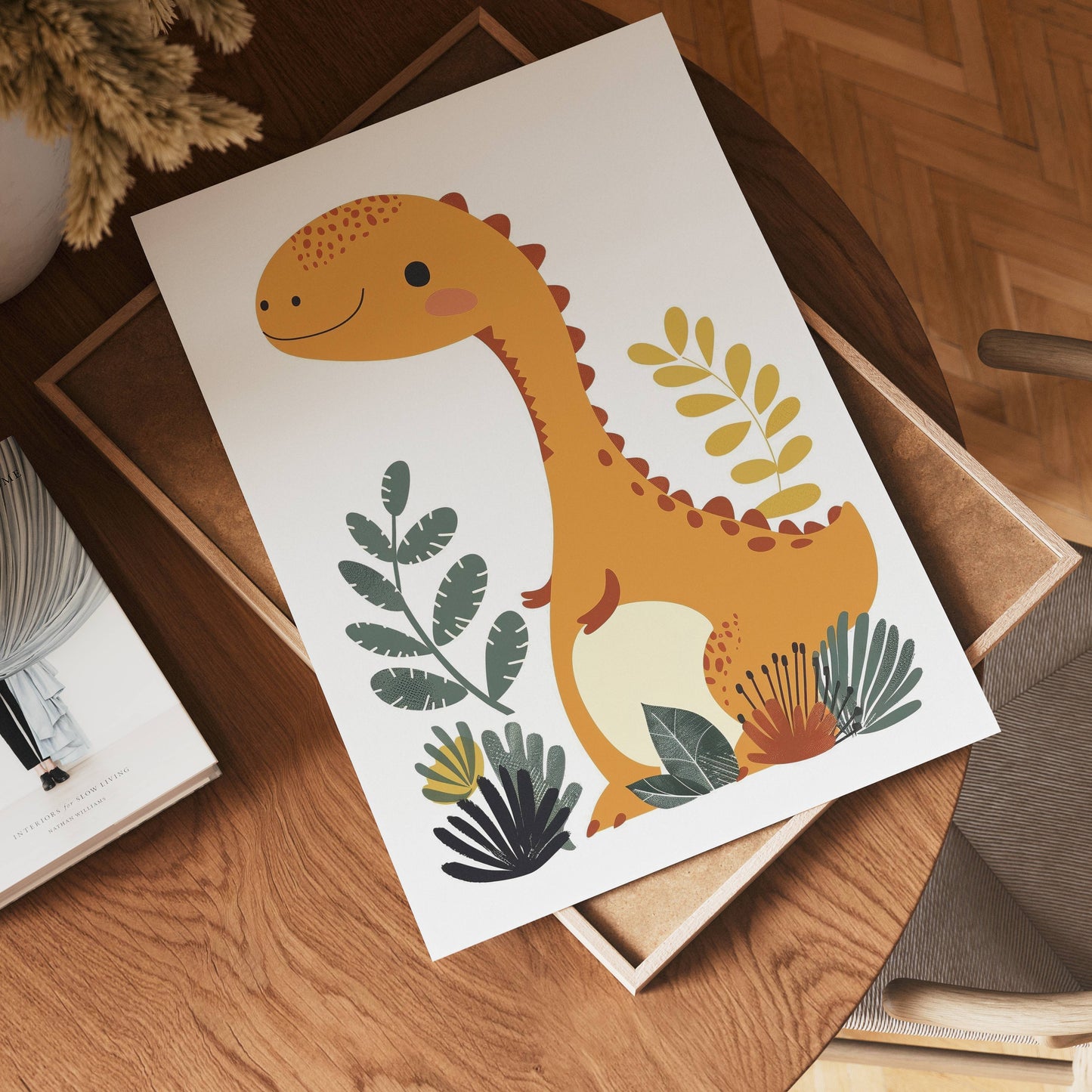 A cheerful orange dinosaur illustration, titled "no-9," stands amid green and yellow leafy plants on a wooden table with books and a chair nearby.