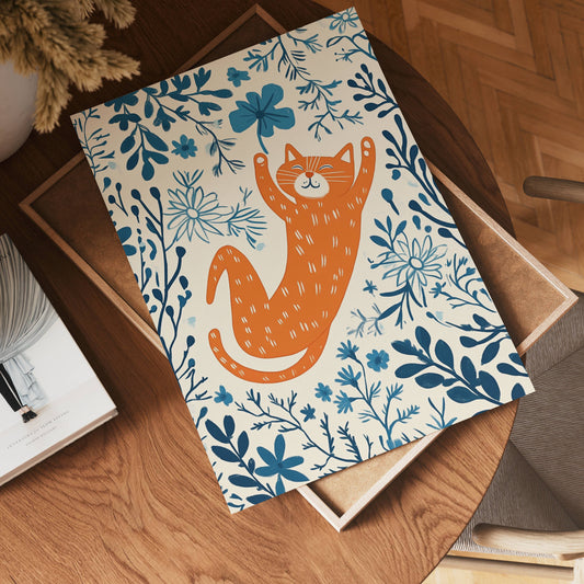 The no-9 features an illustration of an orange cat reaching up playfully amidst blue leaves and flowers, displayed on a wooden table beside a chair and a stack of books.