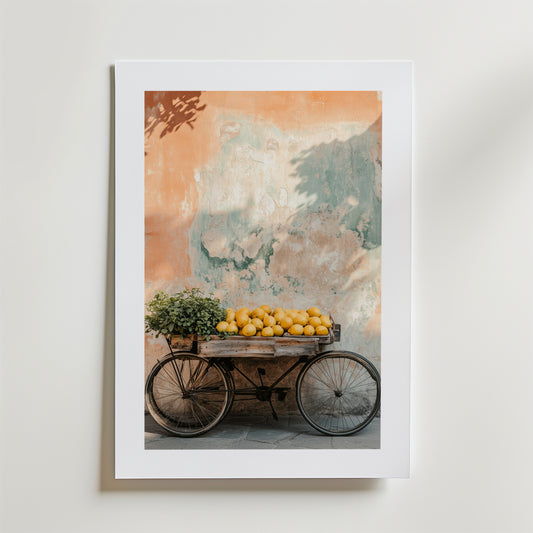 Wheels & Citrus Poster by Bozetto är ett inramat foto på FSC-certifierat premiumpapper som visar en vintage trävagn med citroner och en krukväxt, mot en väderbiten vägg i mjuka orange och gröna nyanser med högkvalitativ finish.