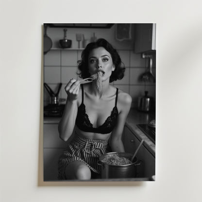 Ett svartvitt foto med en matt yta visar en kvinna i ett kök, klädd i en spetsbralette och randiga shorts, som äter nudlar från en kastrull. Denna Bozetto Spaghetti Vintage Poster framkallar retro charm för din inredning.