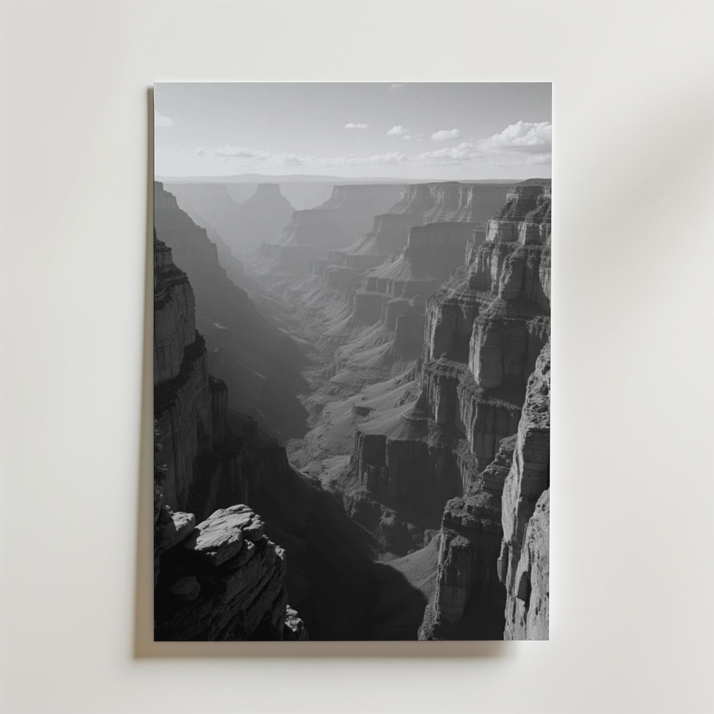 Grand Canyon Shadows Poster by Bozetto: Svartvitt foto med karga klippor och en skuggig dal under en delvis molnig himmel, tryckt på FSC-certifierat premiumpapper med elegant matt yta. Perfekt som Grand Canyon väggkonst.