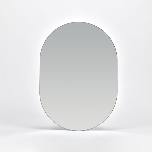 Bozetto Spegel Ark 50x70 cm, en stor ramlös väggspegel med en platt bas, är monterad på en vit vägg och reflekterar en mjuk neutral gradient.