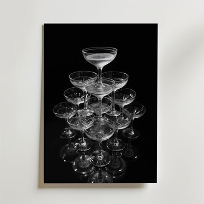 Champagne Glas Pyramid No.2 Drink Poster by Bozetto: Ett snyggt svartvitt foto av en pyramid av champagneglas med vätska i det översta glaset, mot en slät bakgrund - perfekt dekor på premiumpapper.