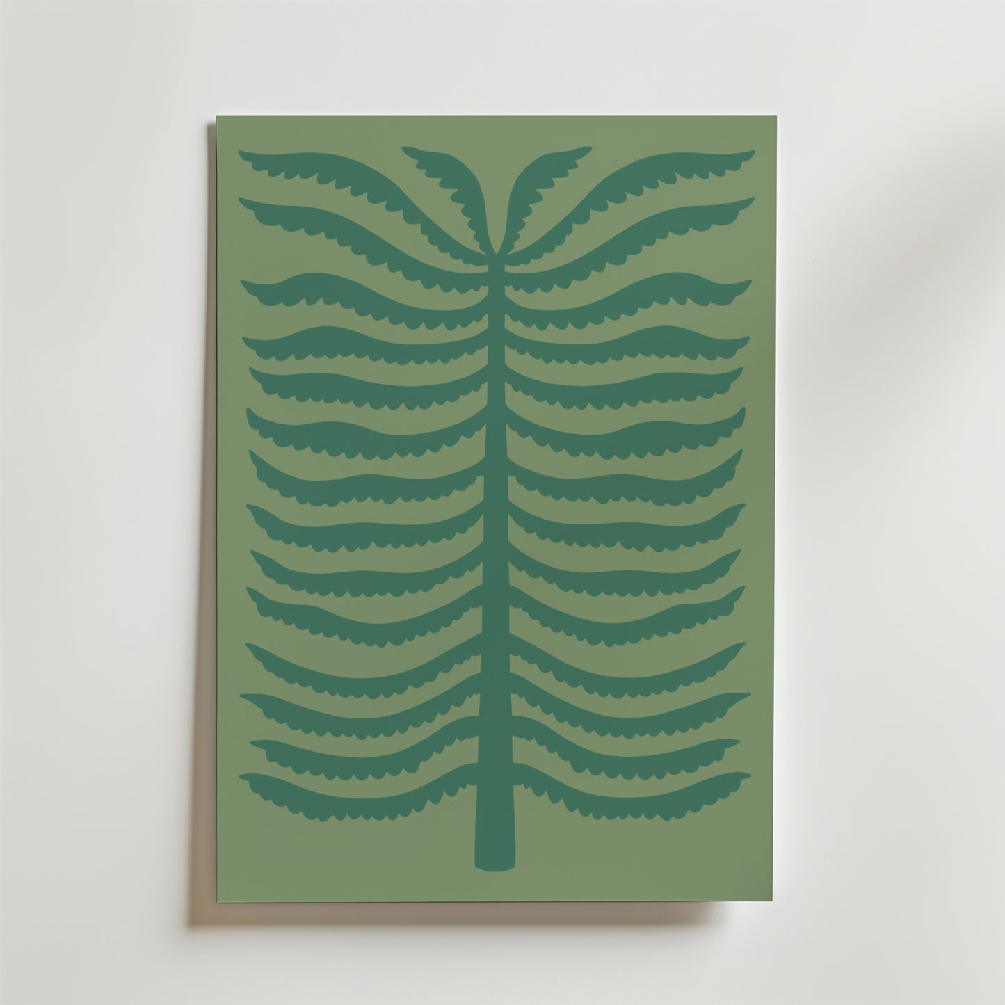 Quiet Palm Poster från Bozetto föreställer en minimalistisk stiliserad ormbunke med mörkgröna symmetriska grenar på en dovt grön bakgrund, inramad och placerad mot en ljus vägg.
