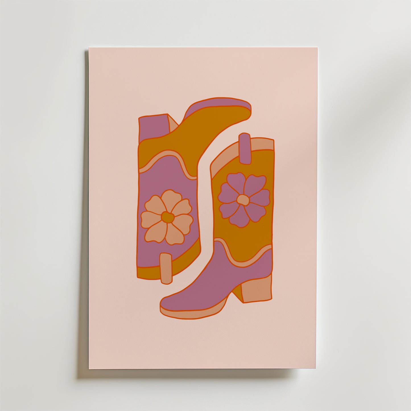 Bozettos "Boots and Blooms Poster" föreställer två blommiga stövlar i orange, rosa och lila med djärva blommönster mot en ljusrosa bakgrund.