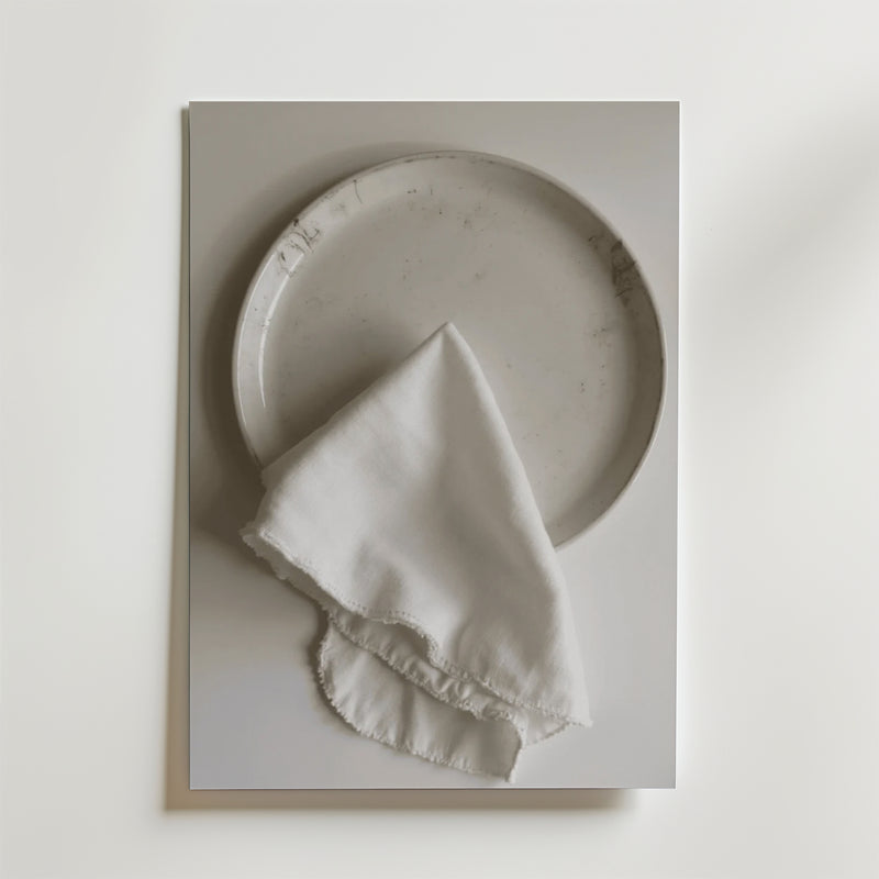 En Bozetto White linen dinner napkin Poster visar en vit keramiktallrik som toppas med en fransig vit linneservett, allt mot en vit bakgrund med en lyxig matt finish.
