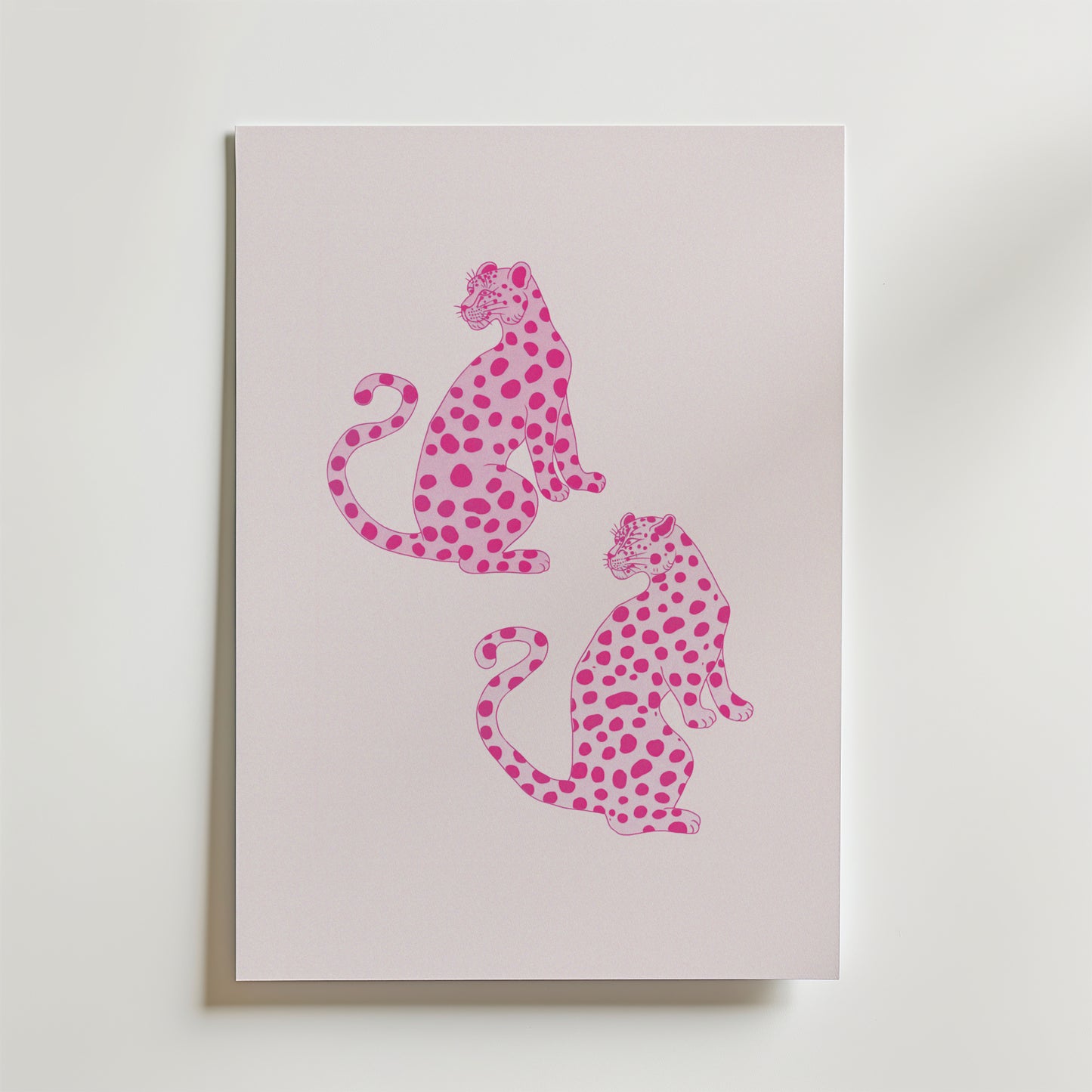 Bozetto Pink Leopard Twins Poster har ett minimalistiskt djurmotiv av två rosa leoparder med mörkare fläckar, som sitter rygg mot rygg på en pastellfärgad bakgrund - perfekt för modern inredning och visas vertikalt på en ljus yta.