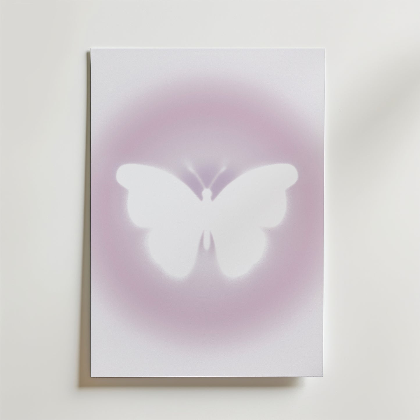 Bozetto's Soft Glow Butterfly Poster visar en vit fjäril i silhuett centrerad mot en ljus, minimalistisk bakgrund med drömskt rosa-lila sken.