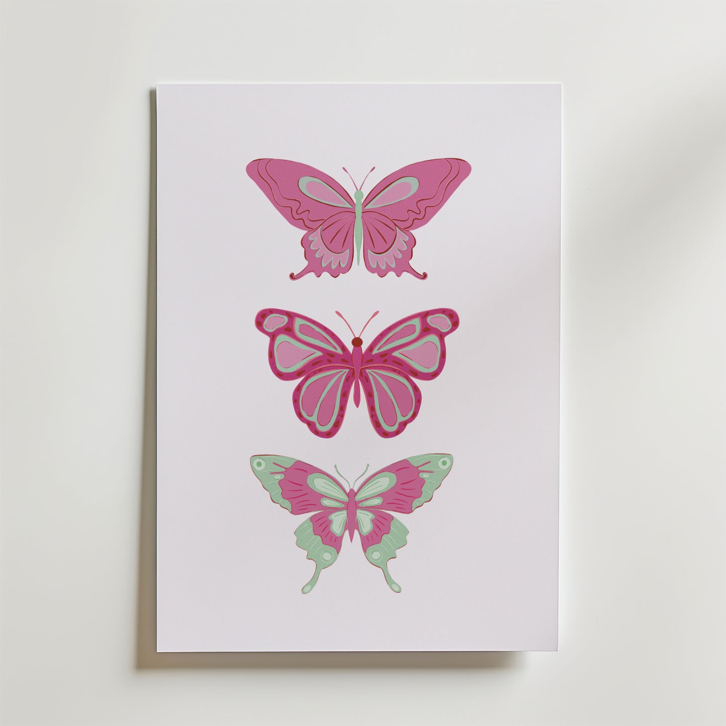 Postern Pink Butterfly Trio Poster från Bozetto föreställer tre illustrerade fjärilar i rosa och mintgrönt staplade vertikalt på en vit bakgrund, vilket framhäver deras unika vingmönster och eleganta skönhet.